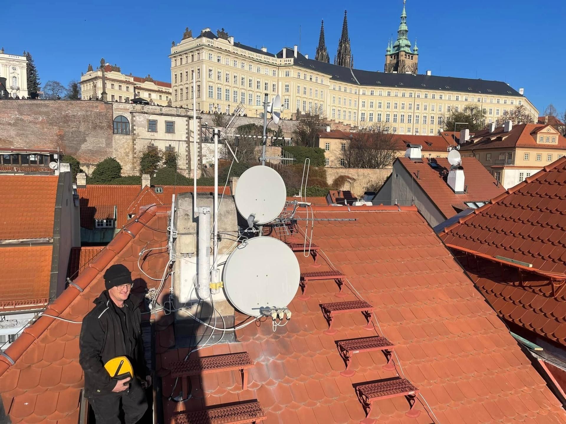 Kominík Kominictví Hlavín na střeše na Malé Straně, v pozadí Pražský hrad